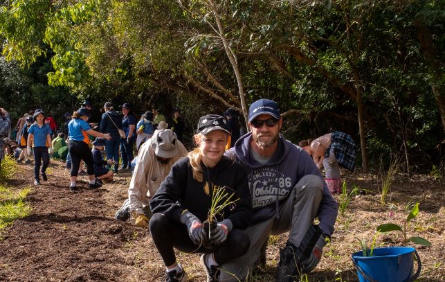 Father and daughter crouched down  planting native seedlings.