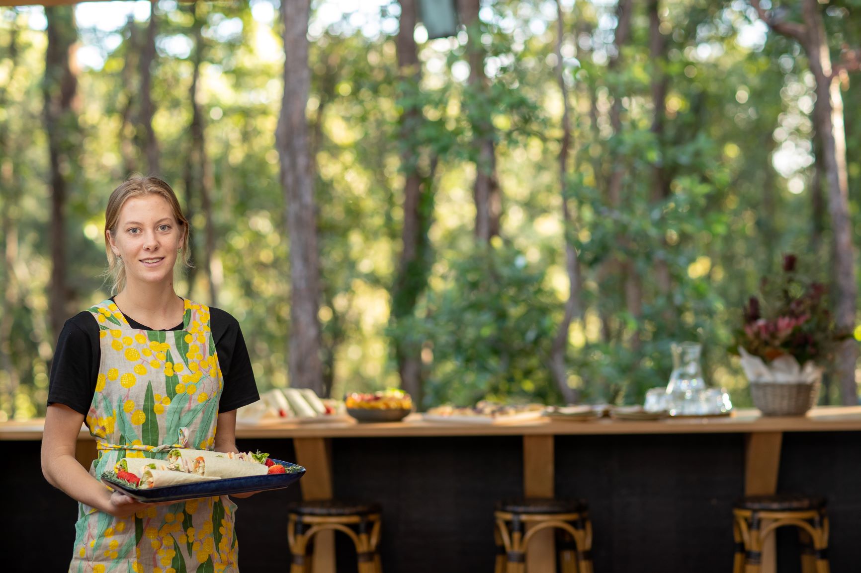 A waiter with a platter of sandwiches ready serve with a bushland background.